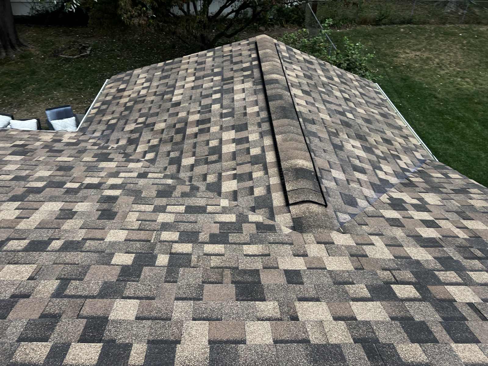 Looking down onto the corner of a hip roof in multi-tone brown shingles, with a black vent strip running down the hip and cap shingles part laid over it
